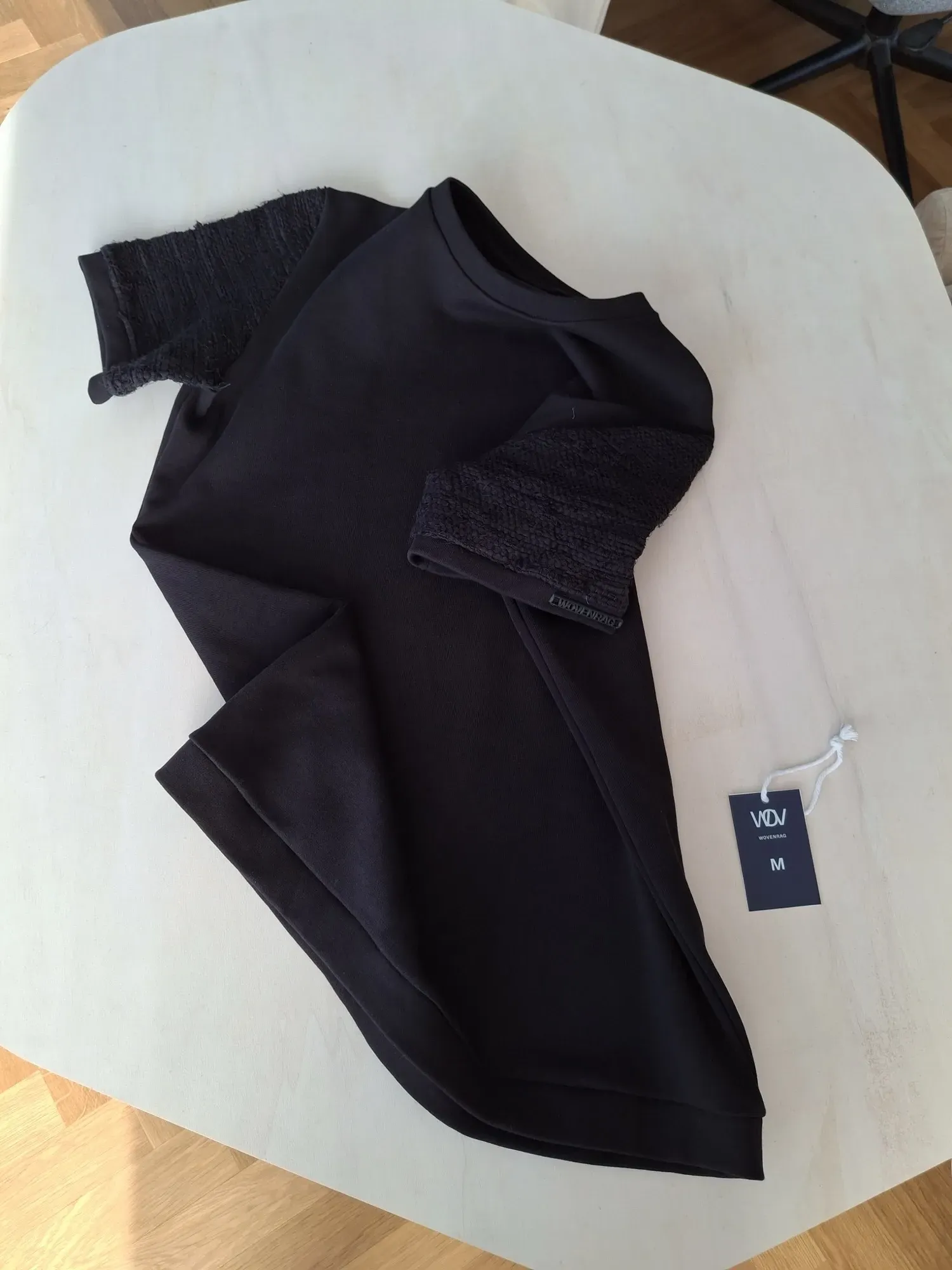 Black Solitaire t-shirt with handwoven sleeves on light table — size M