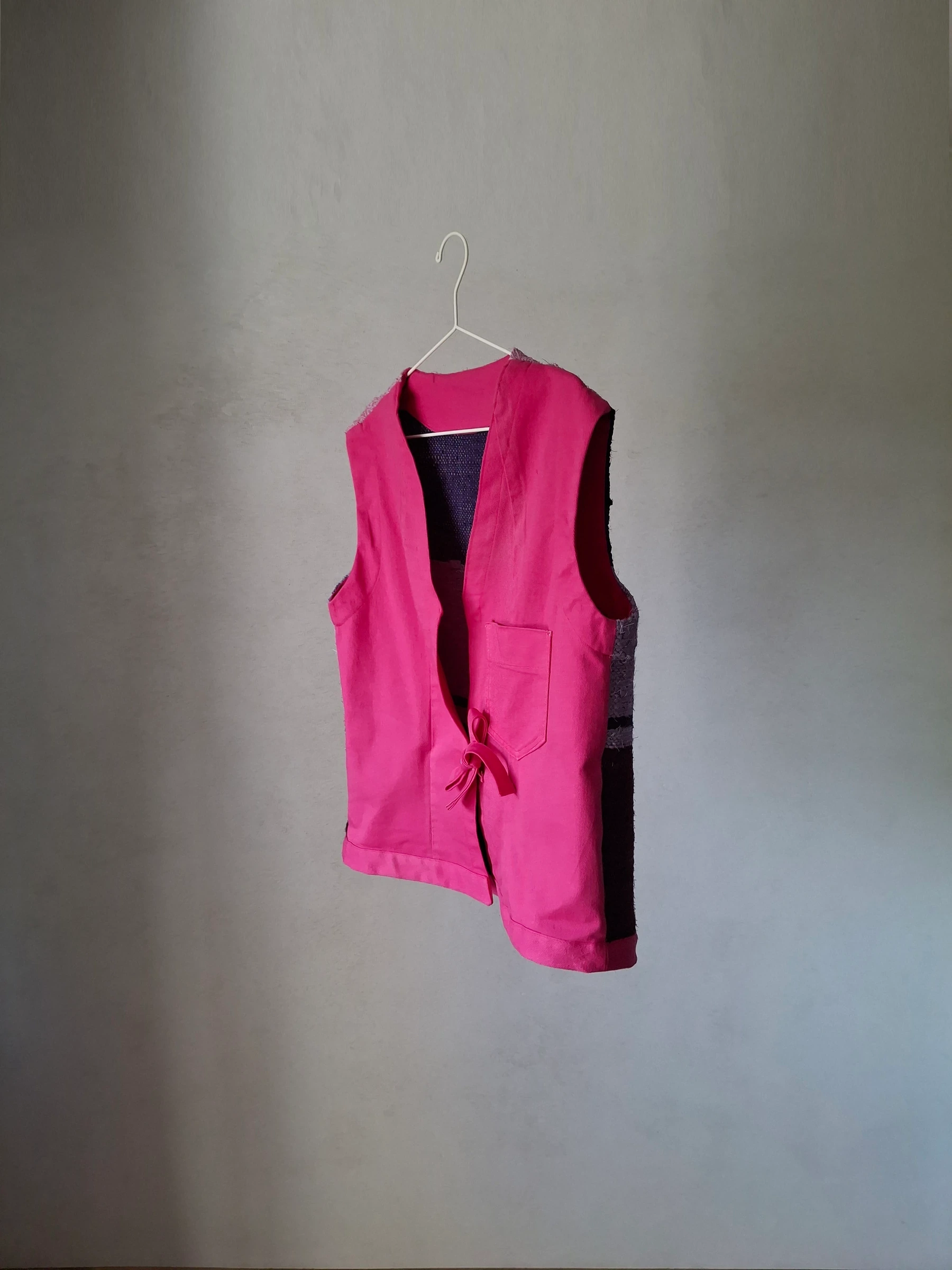 Angled front view of the magenta vest with its fabric-ribbon tie