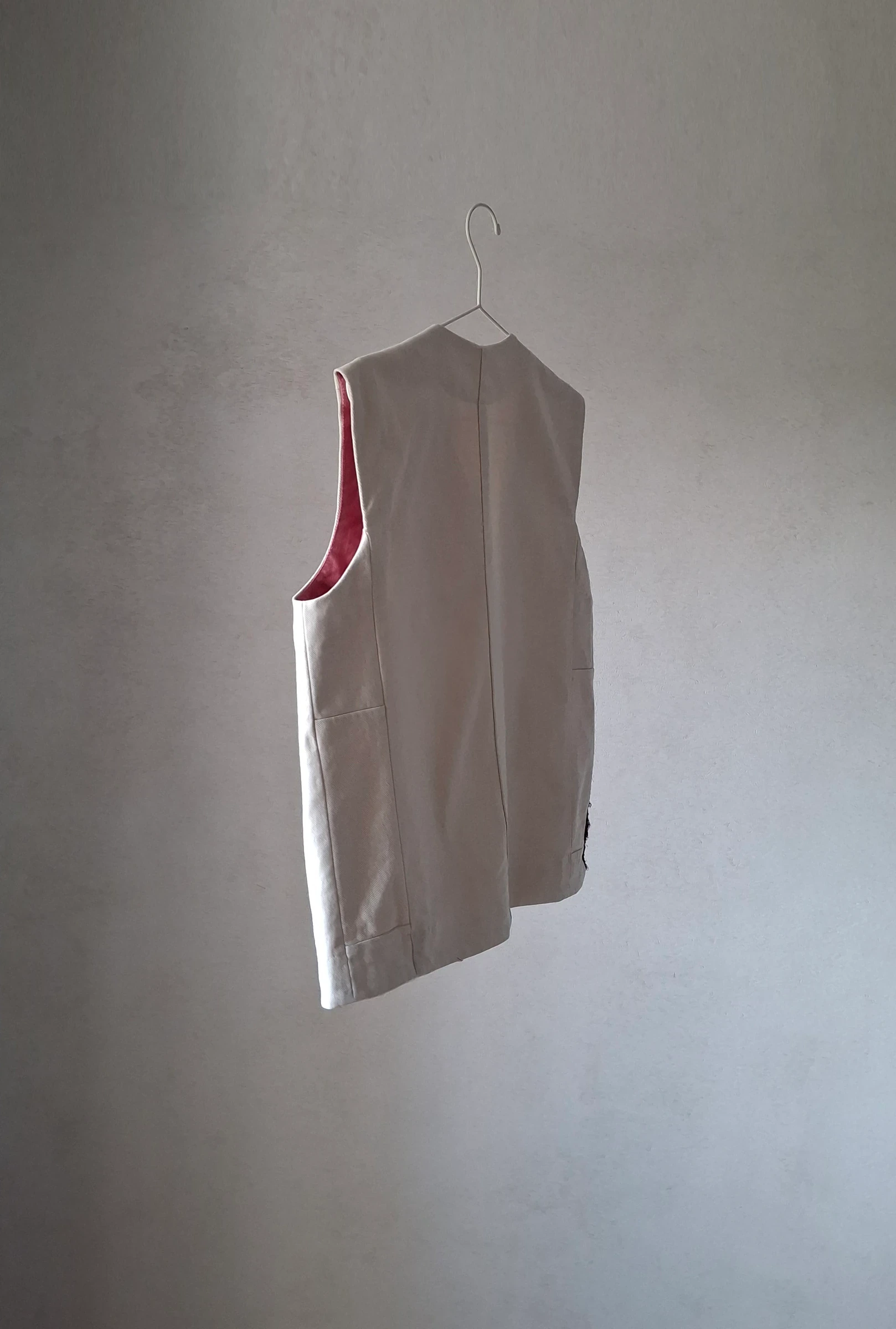 Side view of the off-white vest showing the rose-toned neckline binding